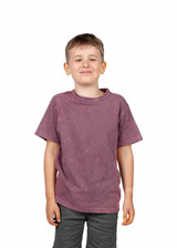 A kid's stone washed t-shirt in a muted mauve colour, displayed on a smiling boy. The shirt features a logo.