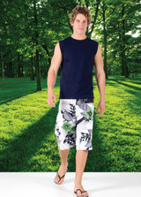 A man wearing a navy muscle T-shirt and floral shorts, standing on a grassy area with trees in the background.
