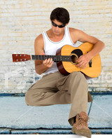 A man in a white cotton rib singlet plays an acoustic guitar, wearing sunglasses and beige pants.