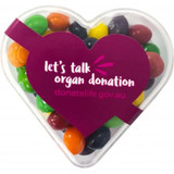 A heart-shaped acrylic container filled with colourful Skittles sweets, featuring a purple label.