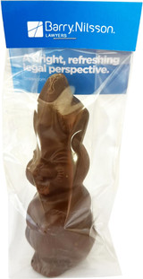 A chocolate Easter bunny in a clear plastic package, featuring a blue header card and a branding logo.