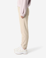 Unisex sweatpants in a light beige colour, featuring a logo, styled with a pink top and white sneakers.