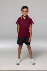 A boy wearing a maroon polo shirt with white trim, paired with black shorts and white sneakers. The shirt has a logo.