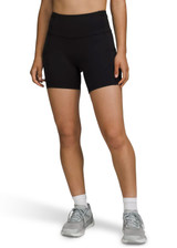 High-rise black legging shorts on a model, paired with grey sneakers. Features a brand logo on the waistband.