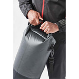 A grey roll-top backpack being secured by a person, featuring a strap and a logo.