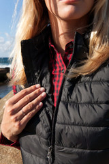 A black puffer vest is partially zipped, worn over a red and black checked shirt. The vest has a logo on it.