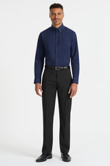 A man stands wearing a navy blue long sleeve button-up shirt and black trousers. The shirt has a logo.