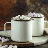 A drinkware set featuring two white enamel cups filled with hot chocolate and topped with mini marshmallows.