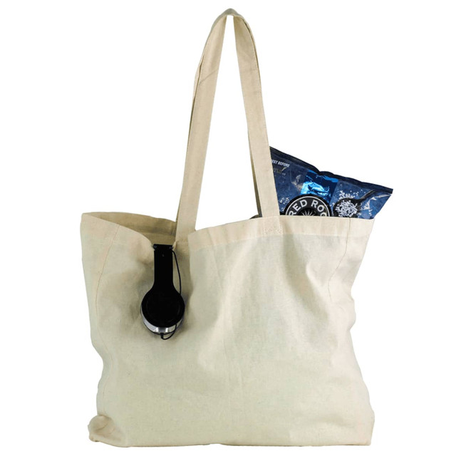 A natural cotton shopper tote in cream, featuring a black headphone and a bag of snacks inside.