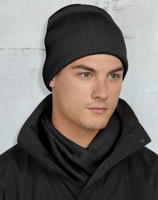 A cable knit beanie in dark green with a fleece headband inside and a logo.