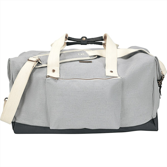 A grey cotton duffel bag with contrasting dark base, featuring two handles and a shoulder strap. It has a front pocket and a logo.