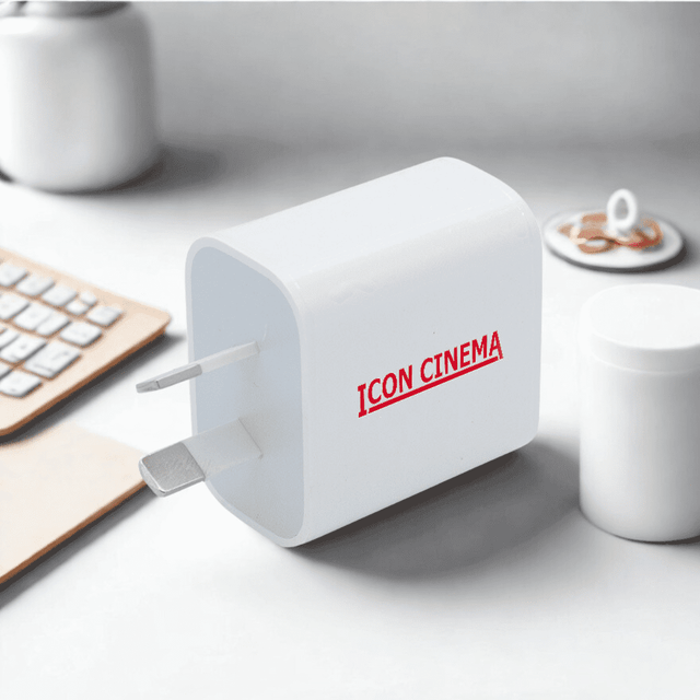 A white travel adapter with a plug and a branding logo, set on a minimalist desk with a keyboard and cup.