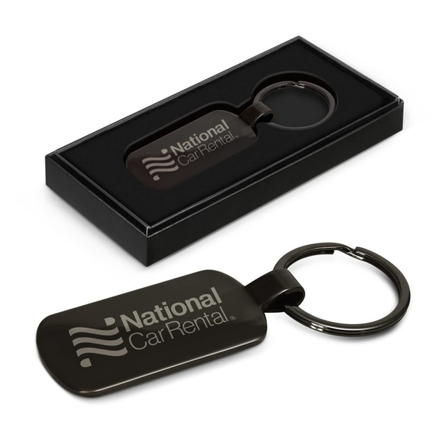 A black Taurus key ring displayed in a black box, featuring a logo. The key ring has a sleek, rectangular design.