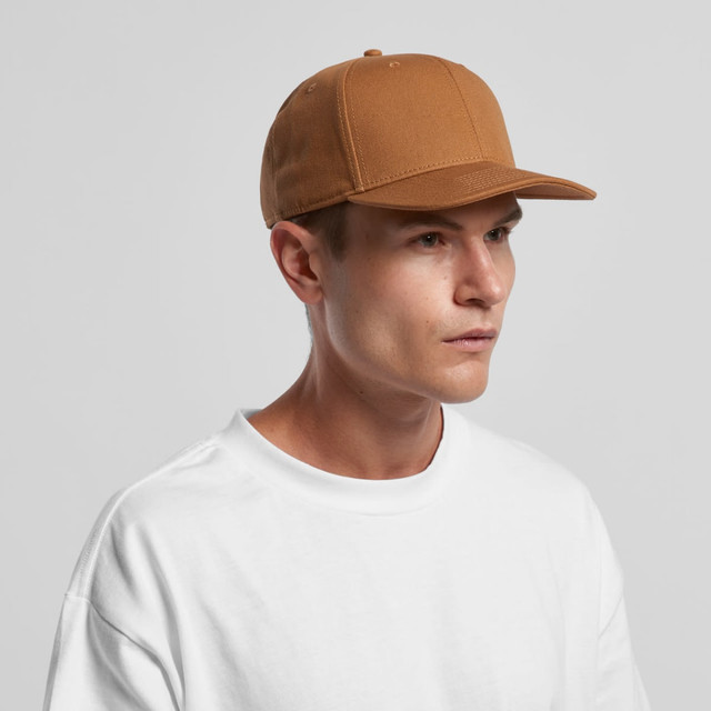 A tan canvas cap with a structured design, featuring a logo on the front, worn by a model in a white shirt.