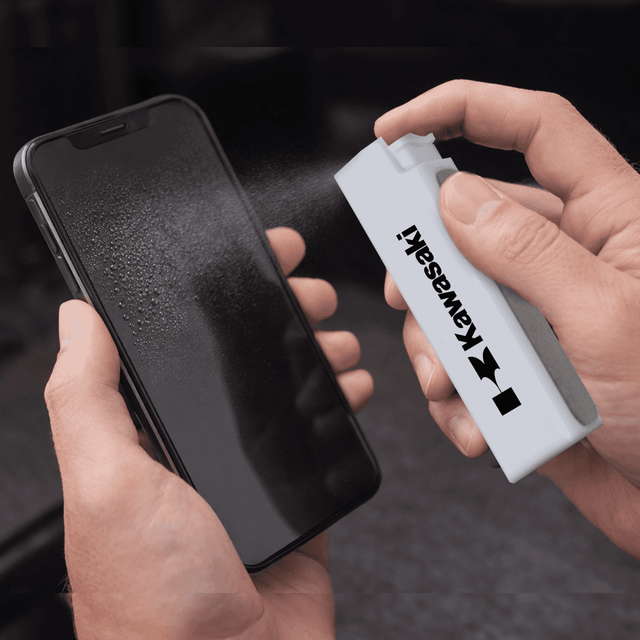 A white spray bottle is cleaning a smartphone screen, which is covered in mist. The bottle has a logo.