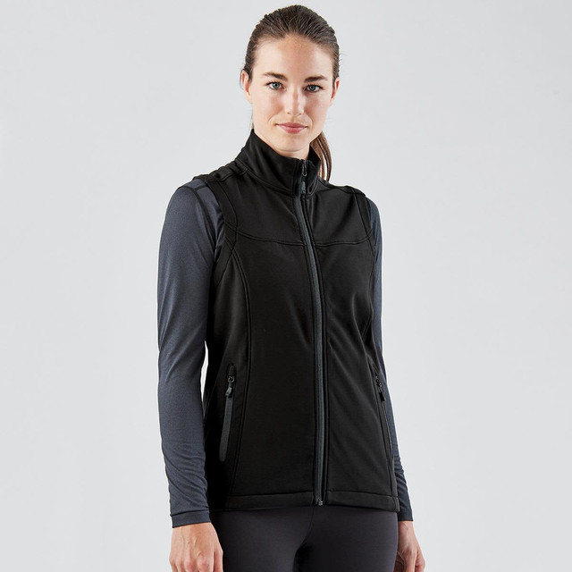 A black softshell vest with a zip front and side pockets, worn over a long-sleeve top. The model has a neutral expression.