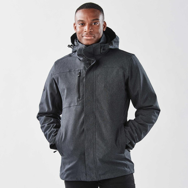 A man wearing a black jacket with a hood, featuring a zipper and pockets, against a plain background.