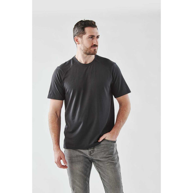 A man wearing a black short sleeve performance T-shirt, styled with casual jeans, against a light grey background.