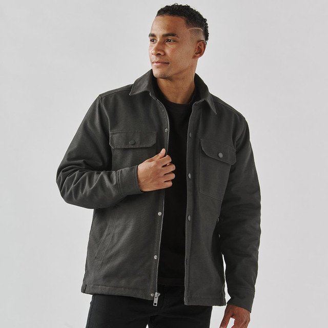 A men's dark grey Sherpa lined canvas jacket with front pockets and a collared neckline. It has a subtle logo.
