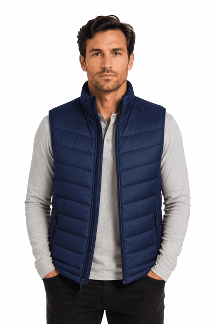 A man models a navy blue puffer vest over a light grey long-sleeve shirt, featuring a branded logo.