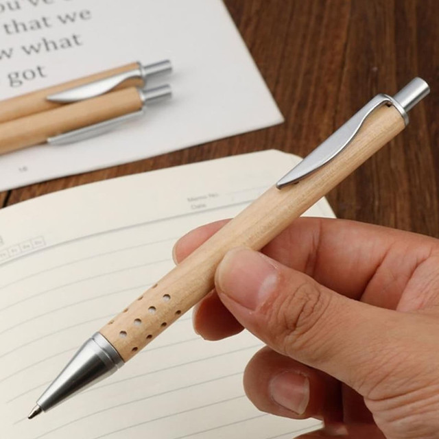 A pen with a wooden body and silver accents, held in a hand above a lined notebook.