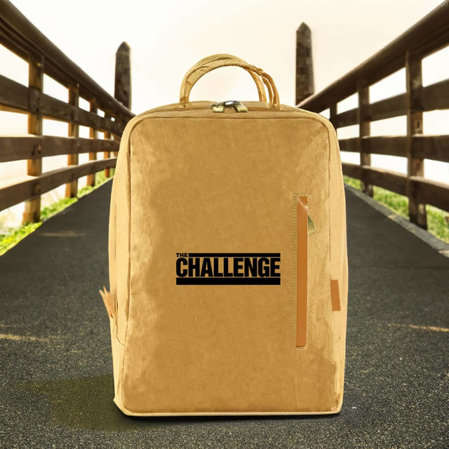 A kraft paper laptop backpack in a tan colour, featuring a logo on the front, set against an outdoor background.