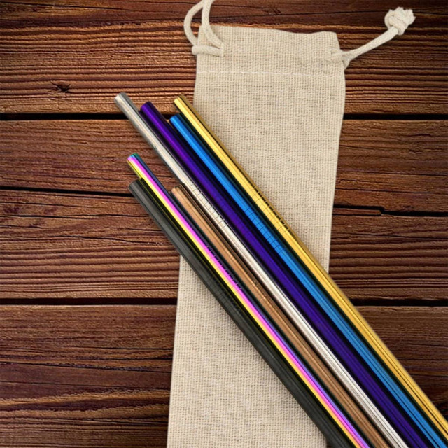 A collection of stainless steel drinking straws in various colours, resting on a canvas bag against a wooden background.