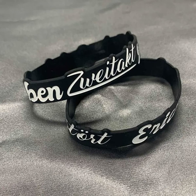 Two black silicone wristbands featuring white custom designs, displayed on a grey background.