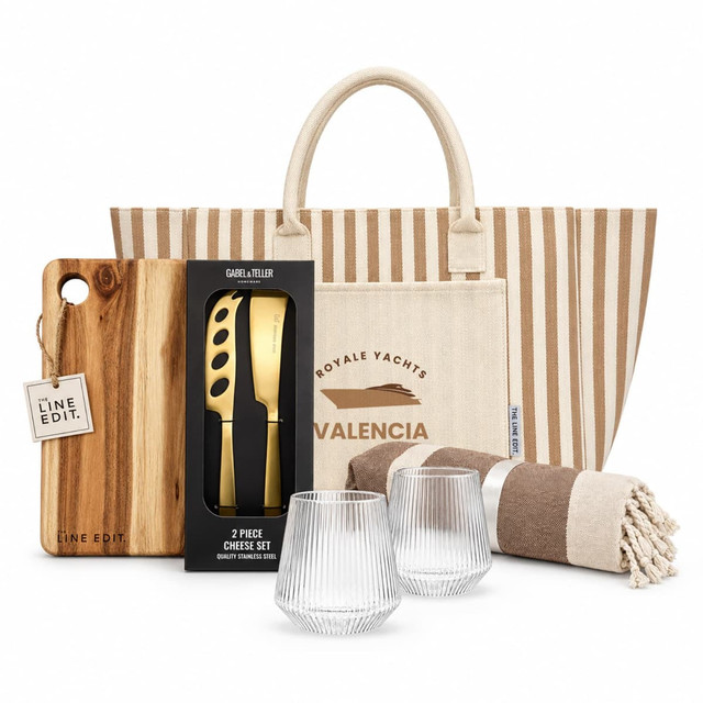 A tote bag with stripes, a wooden cheese board, a two-piece cheese set, two textured glasses, and a striped blanket.