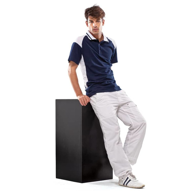 A young man wearing a navy and white polo shirt, paired with white pants, leans against a black pedestal.