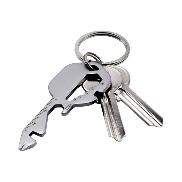 A multi-tool keyring in metallic grey with several standard keys attached. The tool features measuring lines and a unique shape.