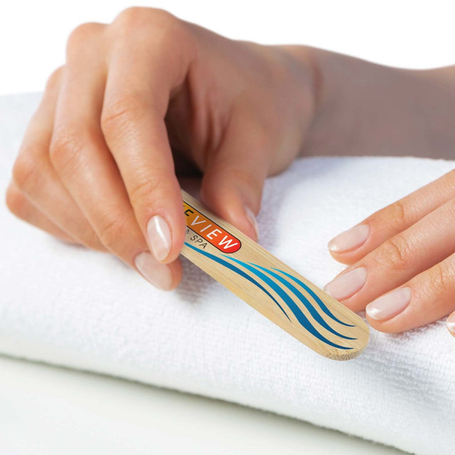A bamboo nail file with a logo, resting on a white towel, held by a hand with manicured nails.
