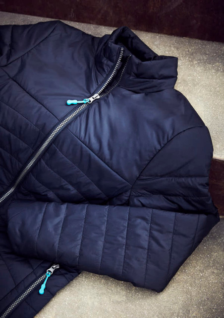 A navy puffer jacket featuring a zip closure and a contrasting zipper pull, displayed on a textured surface.