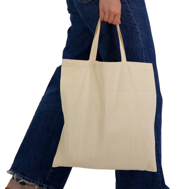 A tote bag in a natural cream colour with short handles, being held by a person wearing blue denim jeans.