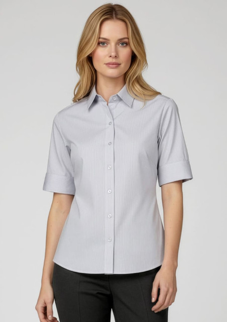 A woman models a short-sleeve button-up shirt in light blue, featuring a collar and a subtle striped pattern.