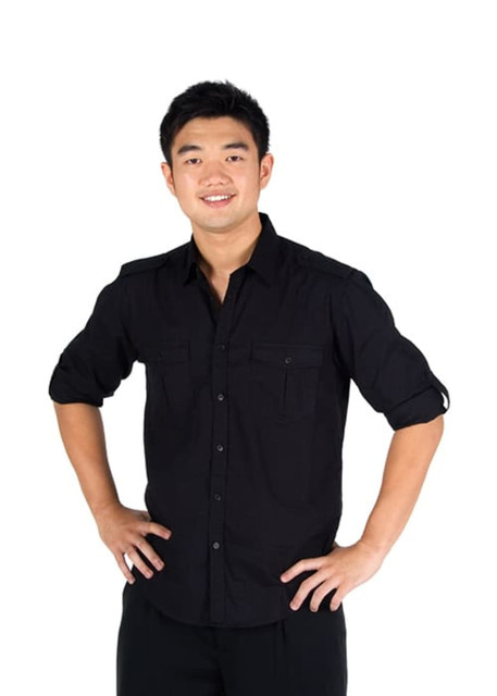 A black long sleeve button-up shirt, worn by a smiling male model, featuring two front pockets and rolled sleeves.