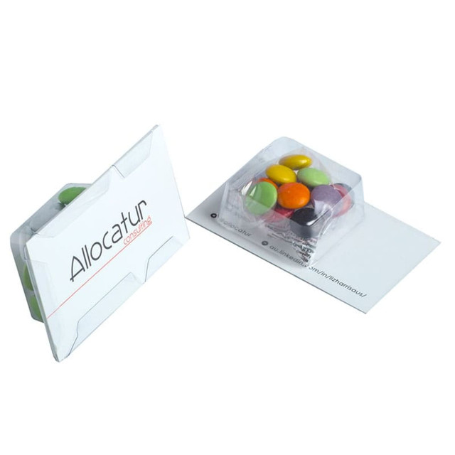 A white promotional card contains a clear plastic tray filled with colourful chocolate beans.