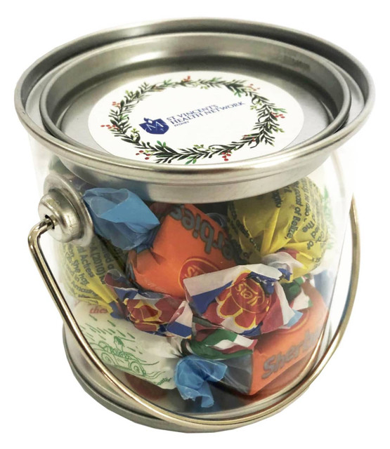 A small clear PVC bucket filled with assorted mixed lollies, featuring a metal handle and a circular label on top.