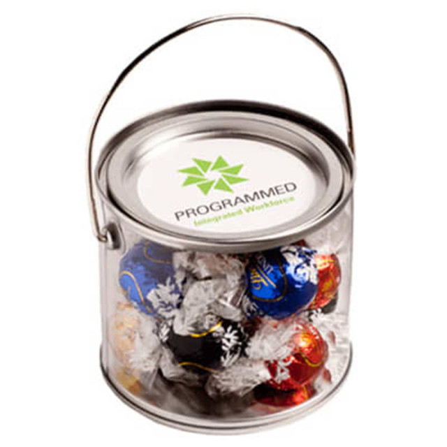 A transparent bucket filled with assorted Lindt chocolate balls in various colours, featuring a metal handle.