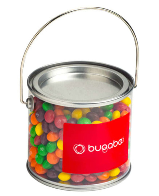 A medium PVC bucket filled with colourful Skittles, featuring a metal handle and a logo.