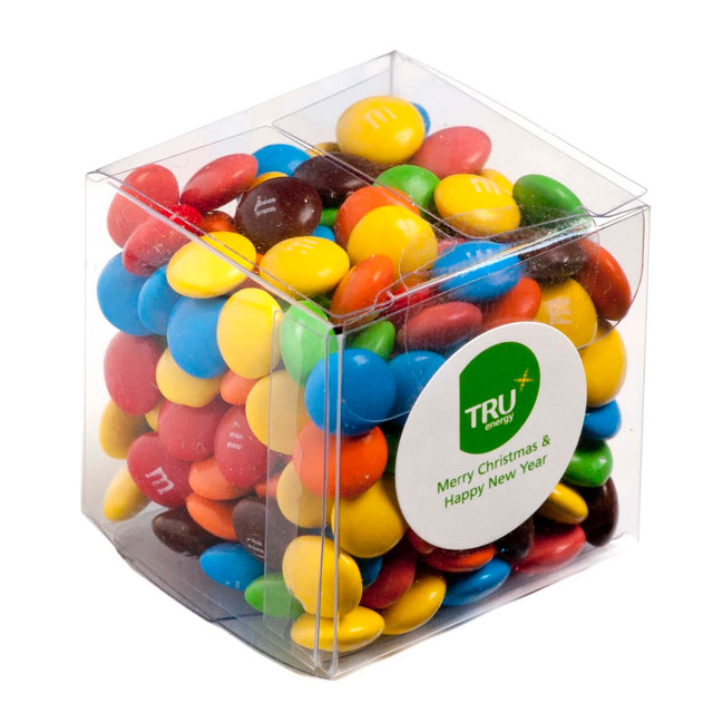 A clear cube filled with colourful M&Ms in various shades, featuring a logo.