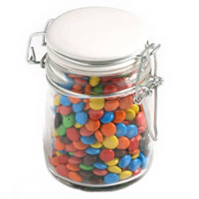 A glass clip lock jar filled with colourful M&Ms in various shades, including blue, red, yellow, and green.