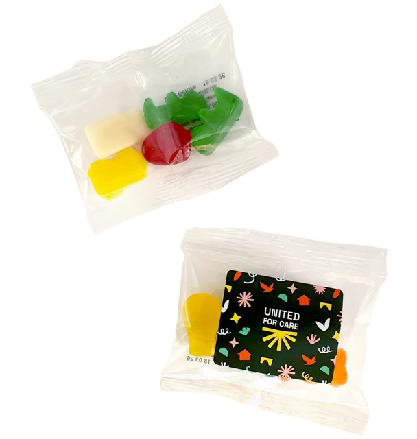 Mixed lollies in a clear bag, featuring yellow, red, green, and white gummy candies. Packaging includes a logo.
