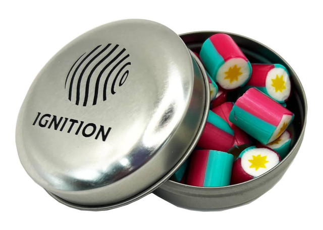 A silver tin contains colourful rock candy pieces in pink, turquoise, and white, featuring a logo on the lid.