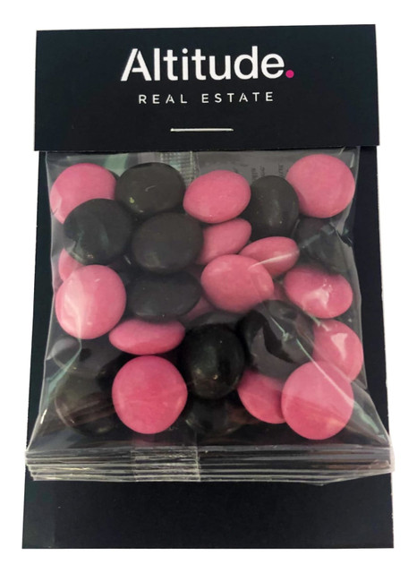 A bag of choc beans featuring pink and dark brown candies, presented in a clear packaging with a branded header.