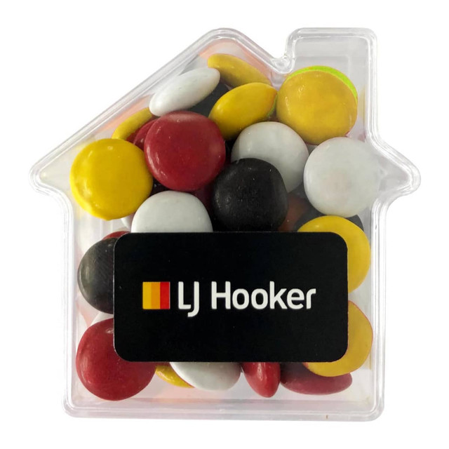 Acrylic house-shaped container filled with colourful choc beans in red, yellow, white, and black. Features a logo.