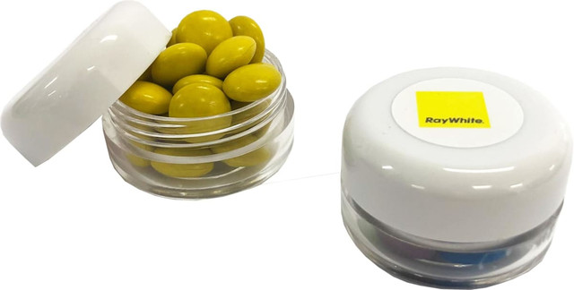 A small clear screw cap jar containing yellow choc beans with a white lid and branding on the top.