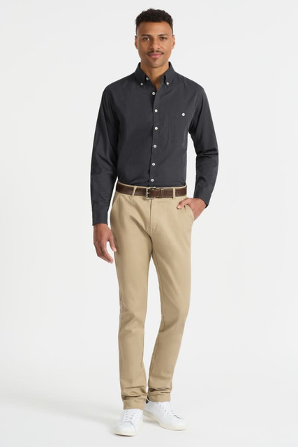 A model wearing a black long sleeve button-up shirt paired with beige trousers and white shoes, featuring a small logo.
