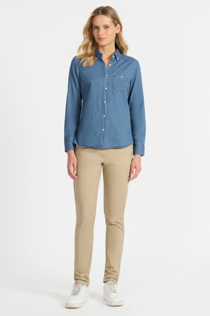 A ladies' long sleeve button-up shirt in denim blue, paired with beige trousers and white sneakers. The shirt has a chest pocket and branding.