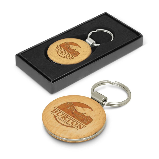 A round wooden key ring with a metal attachment, presented in a black gift box. Features a logo.